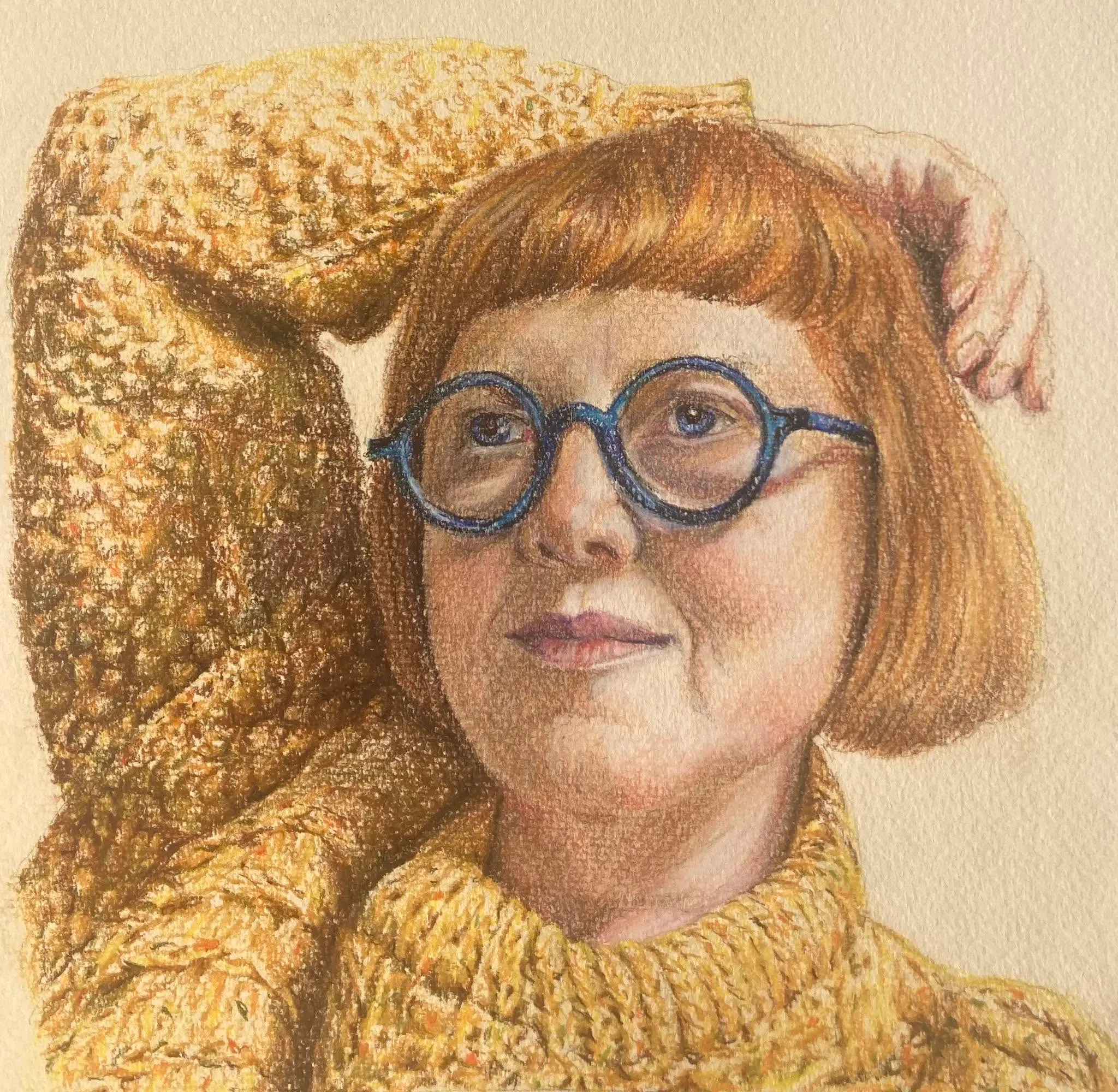 Self-portrait of Marie McCrory with a red bob and round blue glasses, one arm raised behind her head, in a chunky mustard jumper